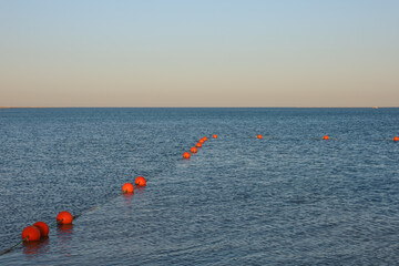 Seascape at sunset. The sun illuminates a line of orange border buoys on blue sea water. Swimming area on the beach