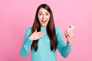 Photo portrait of girl amazed smiling using smartphone hand on chest isolated on pastel pink color background
