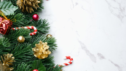 Fototapeta na wymiar Green pine tree leaves, red christmas decorations and candy canes on white marble background, christmas decorations in bright red color. Simple and creative christmas concept.