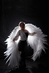 Self-assured adult blonde middle age woman with white angel wings. Model posing in studio on black background. Cupid on Valentine's day