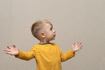 Cute boy in yellow t-shirt blond European German age 3 years isolated on gray background shows and...