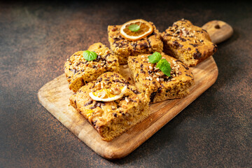 Pumpkin blondie bars with chocolate and walnuts close-up. Brownie pie slices on a serving wooden board on the dark culinary background. Baking for Thanksgiving	