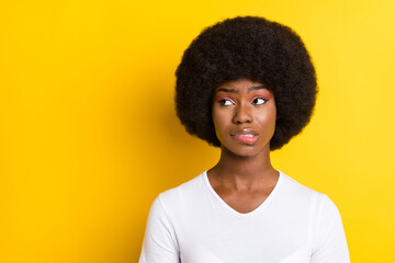 Photo of unhappy troubled young dark skin woman look empty space bite lip isolated on yellow color background