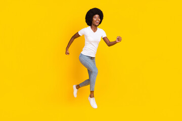 Fototapeta na wymiar Full length photo of pretty sweet dark skin lady wear white t-shirt jumping high running fast smiling isolated yellow color background