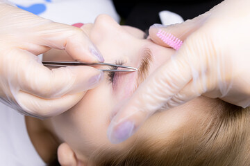 the hands of the master in white gloves stretch the eyebrow and pluck out excess hairs along the...