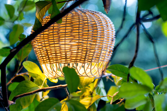 Cute wicker vintage floor lamp in green garden branches. A cozy place for a relaxing stay.