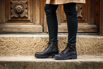 Trendy black boots. Close-up stylish leather shoes. Female legs standing on staircase on street