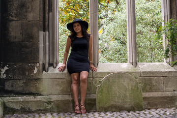 Portrait of Latin woman with wavy hair in black clothes with hat, next to a window