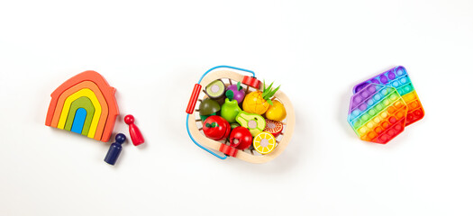 Baby kids toys. Top view to colorful toys arranged on white background. Wooden rainbow house, wooden fruit and vegetables and pop it toys. Leisure entertainment and education for children