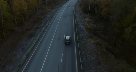 One gray silver crossover SUV car driving alone road trip, travel on freeway through dense colorful forest corridor at autumn sunny sunset - Aerial drone wide view
