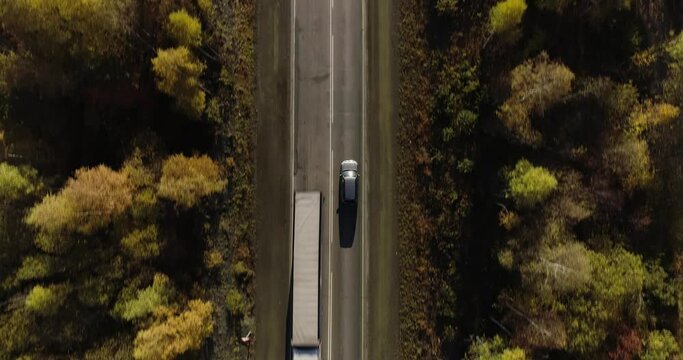 One gray silver crossover SUV car driving alone road trip, travel on freeway through dense colorful forest corridor at autumn sunny sunset - Aerial drone wide view