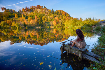 a young and elegant woman who fishes on the shore of a lake in the autumn season