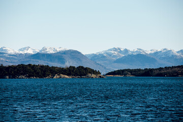 Beautiful scenic view of cold blue sea, island with stony shore and mountains with snowy peaks on the background