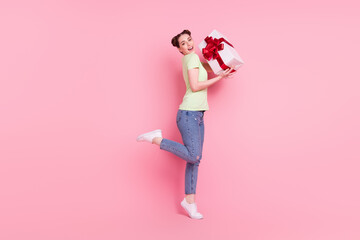 Photo of cheerful charming lady hold present box raise leg wear green t-shirt jeans footwear isolated on pink background