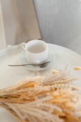 a white cup and a bouquet of dry flowers on the coffee table in the living room