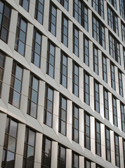 close up perspective detail of tall high rise modern apartment building with geometric metallic cladding and dark windows