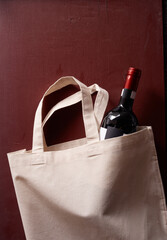 Vertical shot of a bottle of wine in an eco-friendl tote bag on a red background