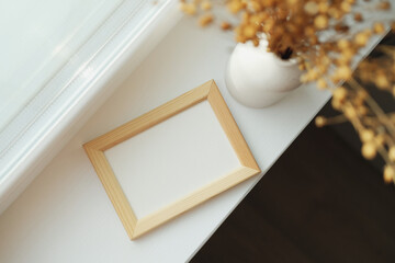 Picture frame mockup and vase of dried linum on windowsill top view. Flat lay, top view, copy space.