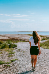 Woman with long brown curly hair walking by the coast of the Baltic sea in Sorve peninsula in Saaremaa, Estonia during sunny and calm day