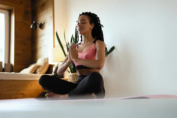 Fotobehang Young black woman doing yoga at home in the lotus position. © opolja