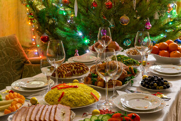 Fototapeta na wymiar Festive Christmas served table against beautiful green pine tree decorated with many colorful new year toys. Xmas dinner, delicious food, christmas turkey. Winter holidays celebration at cozy home