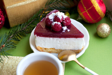 Raspberry cheesecake with cup of tea on green background. New year tea and dessert with christmas decorations.