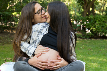 Portrait of affectionate pregnant lesbian couple relaxed at the park. Two happy girlfriends....