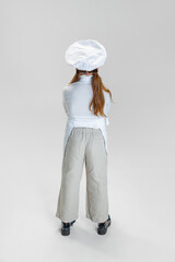 Back view of little girl in white cook uniform and huge chef's hat posing isolated on white studio background.