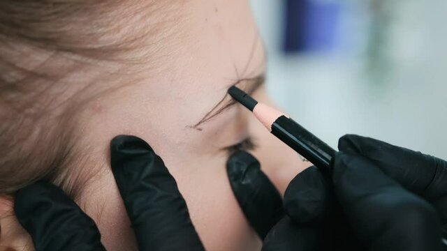 Permanent makeup master drawing right shape of eyebrows for model preparing for microblading
