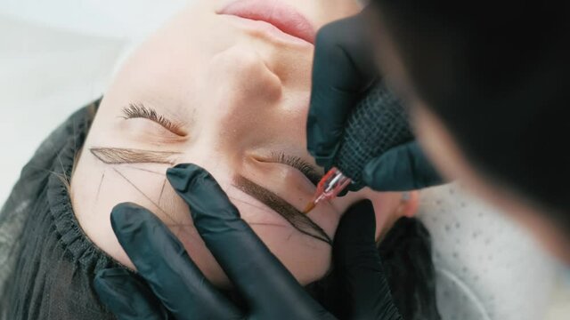 Cosmetologist making eyebrows permanent makeup using ink machine. Microblading tattoo process
