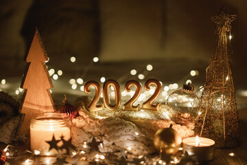 Fototapeta na wymiar Happy New Year 2022. Number 2022 made by candles on a festive sparkling bokeh background in the dark. New Year background with sweaters, garlands and New Year decorations.
