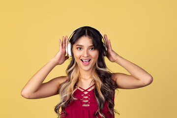 Close-up portrait of young beuatiful girl, student listening to music isolated on yellow studio backgroud.