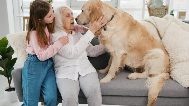 Grandmother and granddaughter sitting on the sofa with golden retriever dog