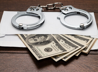 Envelope with dollars on a wooden background. Steel handcuffs on the envelope. The concept of punishment for bribery. Close-up.