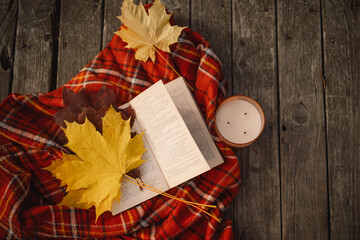 Open book with candle and bouquet of autumn leaves with a plaid on a wooden pontoon. Autumn mood. Read and rest. Cozy autumn concept.