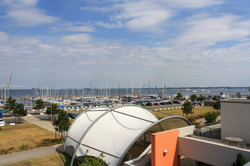 View of sailboats docked at the pier viewed from University of Kiel Sailing Center in summer with clouds in blue sky background.