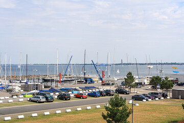 View of sailboats docked at the pier and car parking viewed from University of Kiel Sailing Center in summer with clouds in blue sky background.