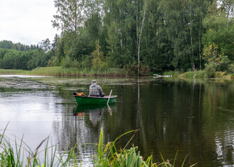 a fisherman in a boat, calm lake water surface, tree reflections, cloudy day, fishing concept