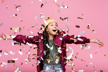 excited preteen girl in stylish outfit smiling near falling confetti on pink.