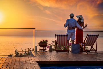 A hugging holiday couple enjoys the beautiful summer sunset over the mediterranean sea with a glass of wine