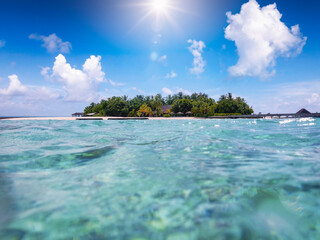 Low angle close to water view to a tropical paradise island with turquoise sea, fine sand and coconut palm trees, Indian Ocean