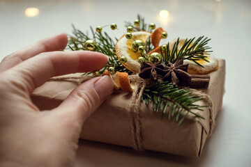 Christmas gift decorated with fresh fir twigs,  dry orange slices and anise stars in human hand