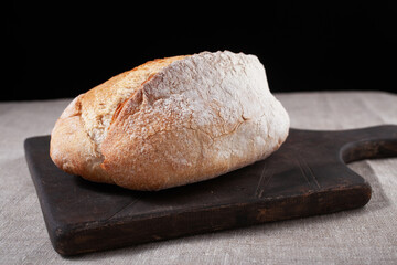 ciabatta of wheat flour on a tree stand close-up on a black background. Baking, flour, bread