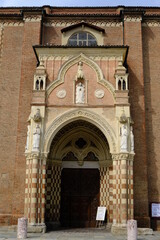 Fototapeta na wymiar Gothic door. Access door to the gothic cathedral of Asti.Portal with marble columns and red terracotta bricks and white marble sculptures. 