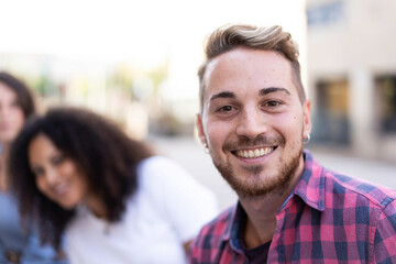 Young man smiling on camera having fun outdoor with multiracial friends in the city - Focus on face