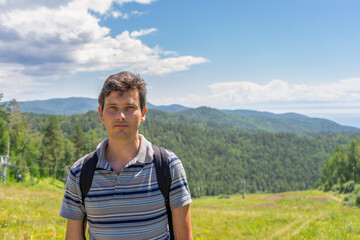 Fototapeta na wymiar Portrait of handsome middle aged tourist man against beautiful mountain landscape in summer sunny day. View from hill to cable way between Listvyanka and Chersky stone. Lake Baikal, Siberia, Russia