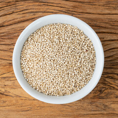 Raw quinoa grains in a bowl over wooden table