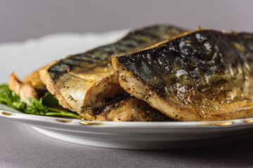 Fried mackerel with a short body file or Platoo in Thai is served on a white porcelain plate on a gray background. Popular fish menu in Thailand. (close-up, side view) 