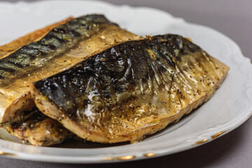 Fried mackerel with a short body file or Platoo in Thai is served on a white porcelain plate on a gray background. Popular fish menu in Thailand. (close-up, side view) 