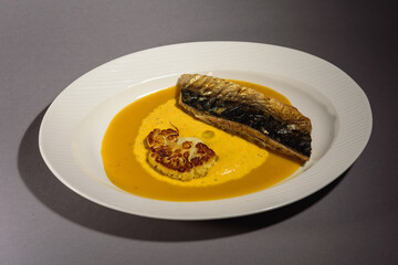 Baked mackerel fish with sauce and cauliflower and yellow puree in a white dish. Fish baked with vegetables. Gray background. Top view.